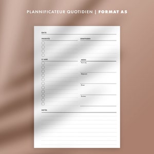 Peut inclure: Un planificateur quotidien blanc avec une bordure noire et le texte "PLANIFICATEUR QUOTIDIEN | FORMAT A5" en haut. Le planificateur comprend des sections pour la date, les priorités, les reconnaissances, les choses à faire, les notes et la planification des repas.
