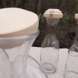 Könnte beinhalten: Drei durchsichtige Glasflaschen mit Korkverschlüssen. Die Flaschen stehen auf einer weißen Oberfläche. Die Flaschen sind leer.