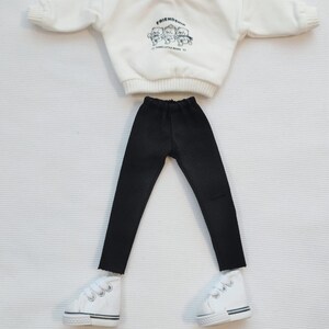 May include: A white doll outfit set with a white sweatshirt that says "Friendship" with three little bears on it, black pants, and white sneakers.