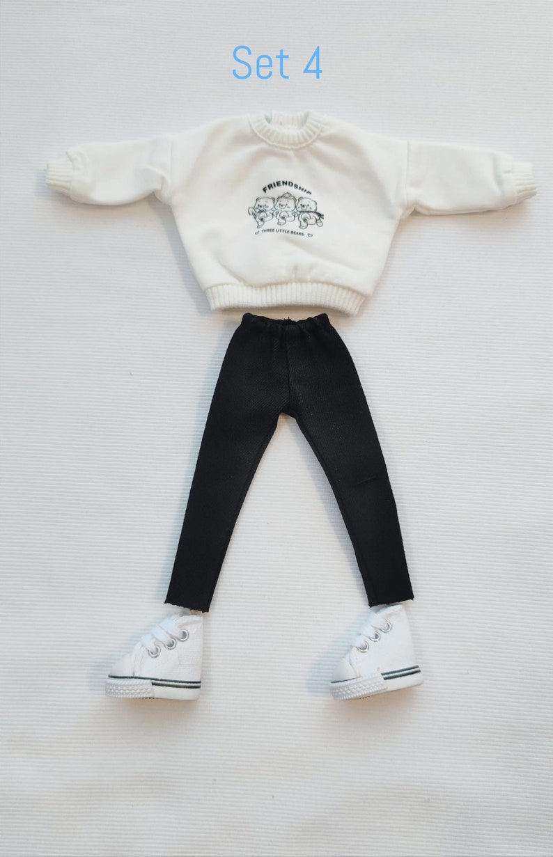 May include: A white doll outfit set with a white sweatshirt that says "Friendship" with three little bears on it, black pants, and white sneakers.