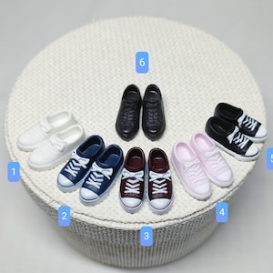 Könnte beinhalten: Zehn Paare Miniatursneaker in verschiedenen Farben, darunter Weiß, Schwarz, Blau, Rosa und Burgunderrot. Die Sneaker sind in zwei Reihen zu fünf auf einer weißen Oberfläche angeordnet.