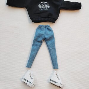 May include: A black sweatshirt with a white graphic of three cartoon bears with the word "Friendship" above them.  The sweatshirt is paired with blue denim jeans and white sneakers.