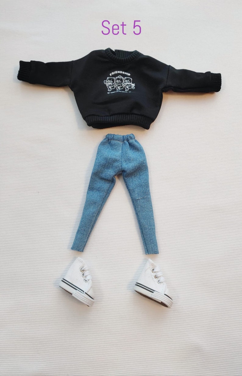 May include: A black sweatshirt with a white graphic of three cartoon bears with the word "Friendship" above them.  The sweatshirt is paired with blue denim jeans and white sneakers.