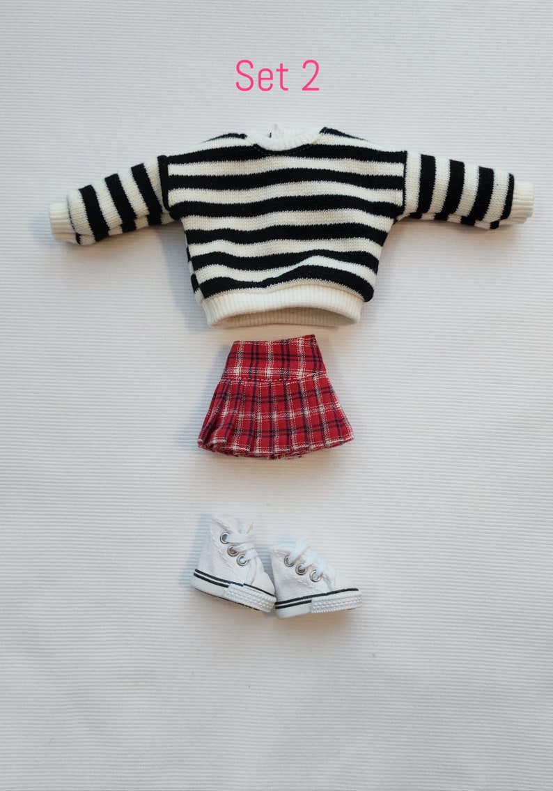 May include: Set 2 of doll clothes includes a black and white striped sweater, a red and black plaid skirt, and a pair of white sneakers.