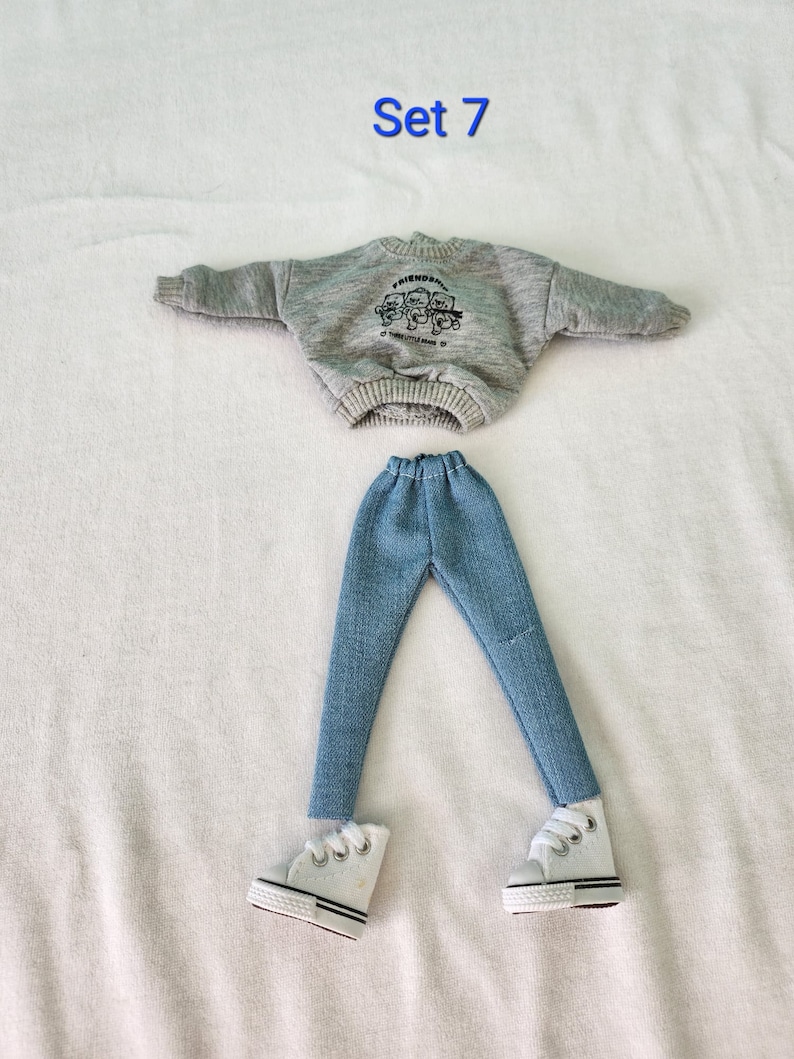May include: A gray sweatshirt with the text "FRIENDS" and a graphic of three bears. The sweatshirt is paired with blue jeans and white sneakers. The text "Set 7" is written above the outfit.