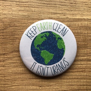 May include: A white button with a green and blue illustration of the Earth and the text "Keep Earth Clean It Isn't Uranus".