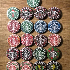 Peut inclure: Une collection de 20 badges ronds de 5,7 cm de diamètre avec différents motifs sur le thème de Noël. Les motifs comprennent le logo Starbucks avec différents textes sur le thème de Noël tels que "Joyeux Noël", "Ambiance de Noël", "Salutations de saison", "Carburant de vacances", "Joyeux Noël", "C'est la saison", "Barista joyeux et festif", "Les vrais meilleurs amis de Noël" et "Joyeux Grinchmas".