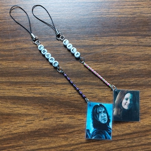 May include: Two handmade phone charms. One charm features a photo of a man with the name "SNAPE" spelled out in white letter beads. The other charm has a photo of a woman with the name "LILY" in white letter beads.