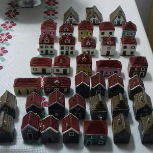 Może przedstawiać: Kolekcja miniaturowych domk&oacute;w z czerwonymi, białymi i brązowymi dachami. Domki są wykonane z r&oacute;żnych materiał&oacute;w, w tym drewna i ceramiki. Są ułożone w grupie na białym tle.