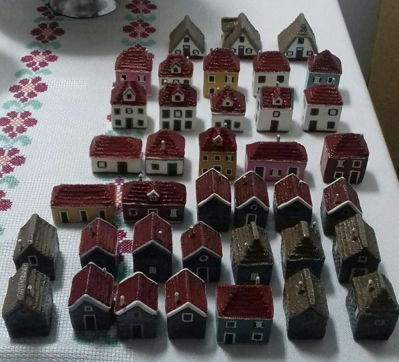 Może przedstawiać: Kolekcja miniaturowych domk&oacute;w z czerwonymi, białymi i brązowymi dachami. Domki są wykonane z r&oacute;żnych materiał&oacute;w, w tym drewna i ceramiki. Są ułożone w grupie na białym tle.