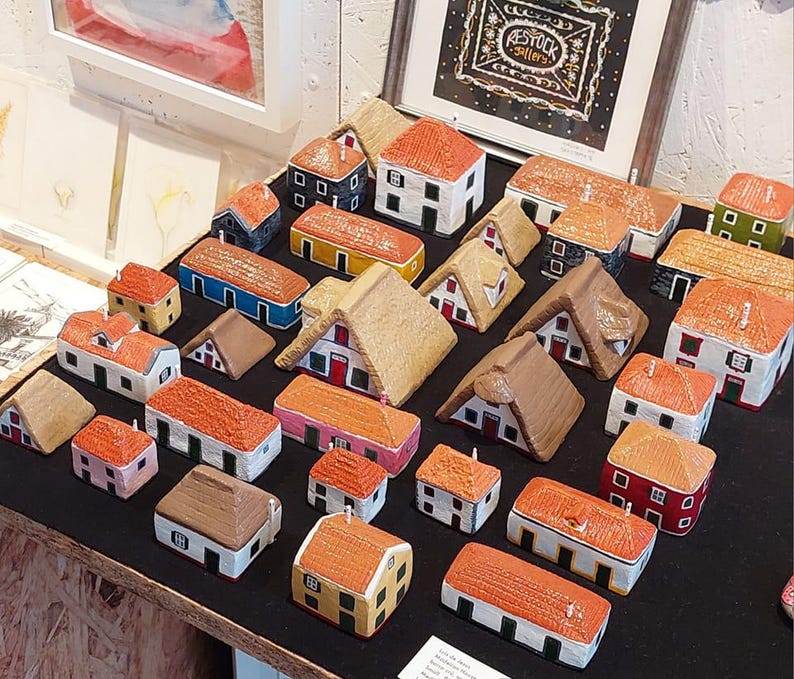 Może przedstawiać: Kolekcja miniaturowych domk&oacute;w wykonanych z malowanego gipsu, każdy z unikalnym wzorem i kolorystyką. Domki są ułożone na czarnej powierzchni, tworząc uroczy i fantazyjny pokaz.