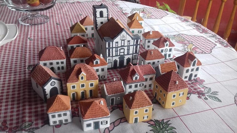 Może przedstawiać: Kolekcja miniaturowych domk&oacute;w ceramicznych w r&oacute;żnych stylach i kolorach, w tym duży kości&oacute;ł z biało-czarną fasadą. Domki są ułożone na szachownicy.
