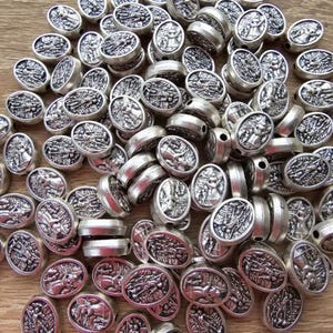 May include: A large quantity of silver oval-shaped beads with a raised design. The beads have a textured surface and appear to be made of metal.