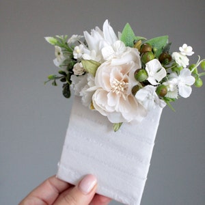 May include: A white envelope with a small bouquet of white flowers and green berries on top.