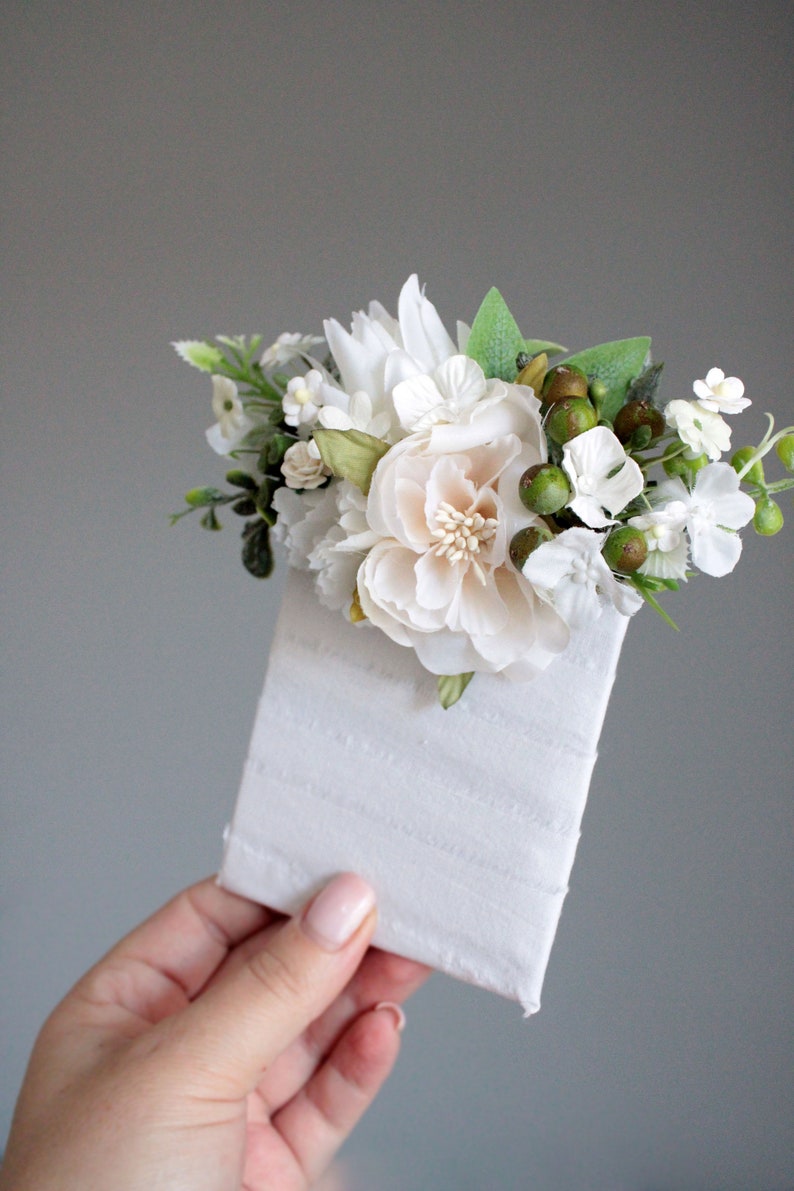 May include: A white envelope with a small bouquet of white flowers and green berries on top.