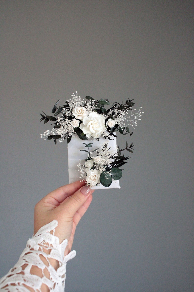 White and greenery pocket boutonniere held in hand, minimalist photo on gray background.