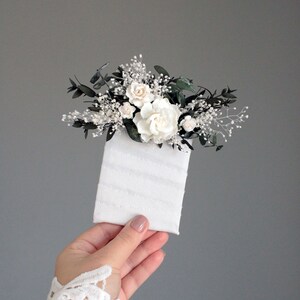Close-up of white rose boutonniere with eucalyptus leaves and baby's breath detail.