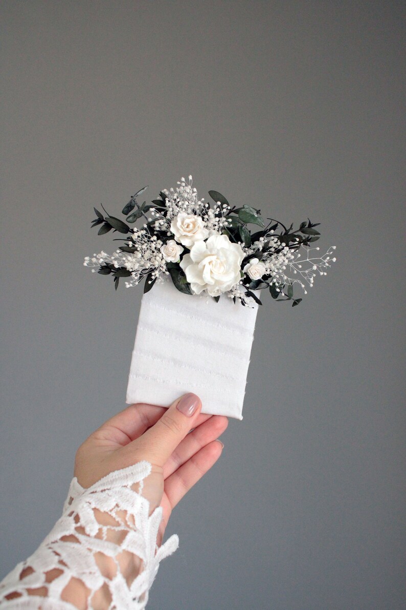 Close-up of white rose boutonniere with eucalyptus leaves and baby's breath detail.