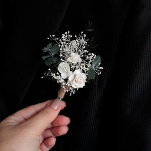 Elegant white boutonniere pinned to black suit lapel, wedding accessory for groom.
