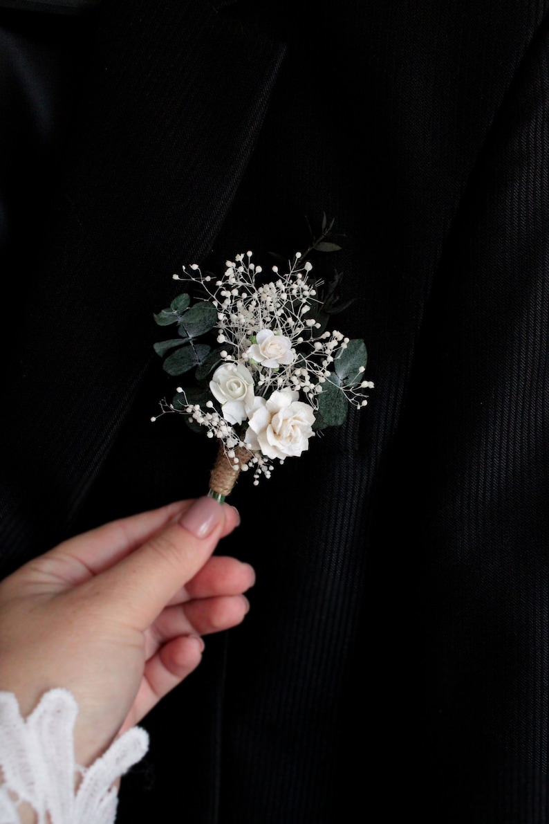 Elegant white boutonniere pinned to black suit lapel, wedding accessory for groom.