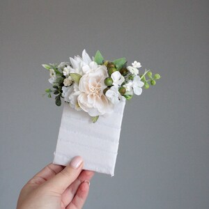 May include: A small bouquet of white and green flowers with a single larger white flower in the center, arranged on a white card.