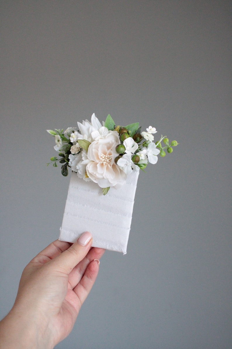 May include: A small bouquet of white and green flowers with a single larger white flower in the center, arranged on a white card.
