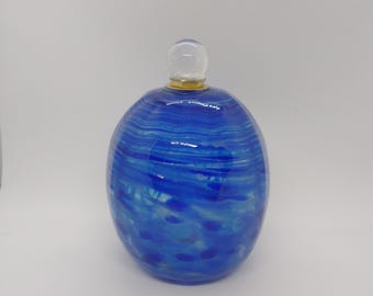 May include: A blue glass decorative bottle with a clear glass stopper. The bottle has a round shape with blue swirls and a gold-coloured band at the top. The stopper is clear and round.