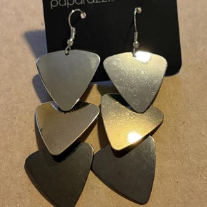 Könnte beinhalten: Ohrringe mit silbernen, goldenen und schwarzen Schichten in dreieckigem Design. Die Ohrringe hängen an einem schwarzen Etikett mit dem Wort "paparazzi". Die Ohrringe sind etwa 5 cm lang.
