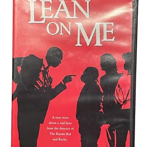 May include: DVD case for the movie "Lean on Me" with a red background and black silhouettes of people. The title "LEAN ON ME" is in large white letters. Text below reads "A true story about a real hero from the director of The Karate Kid and Rocky."