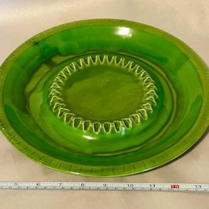 May include: A bright green ceramic ashtray with a circular center and a ridged edge. The ashtray has a glossy finish and a series of notches around the inner circle. The outer rim has a textured design.