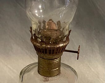 May include: A clear glass oil lamp with a white and gold base. The base is decorated with a pattern of eagles. The lamp is approximately 18 cm tall.