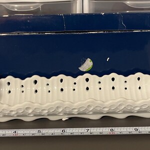 Può includere: Piatto da portata in ceramica bianca con un bordo decorato a festoni e un design a taglio. Il piatto è lungo circa 25 cm.