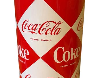 May include: A red and white Coca-Cola can-shaped container. The container features a diamond pattern with the Coca-Cola logo and the word "Coke" in white. The top and rim are silver.