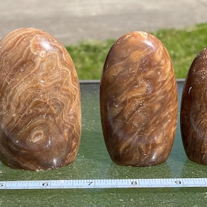 May include: Five smooth, polished, brown and white banded, oval-shaped, natural stone eggs. The stones are arranged in a row from largest to smallest.