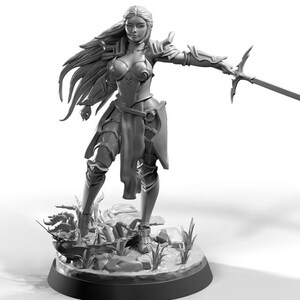 May include: A monochrome figurine of a female warrior in armour, holding a sword. The figure has long flowing hair and is posed on a small, detailed base with rocks and foliage. The armour includes shoulder pads, chest protection, and leg guards.