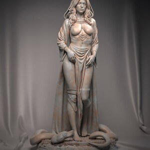 May include: A detailed sculpture of a woman with long hair, wearing a draped garment and jewelry. A rose adorns her hair. A snake is at her feet. The statue is in a neutral color and stands on a textured base.