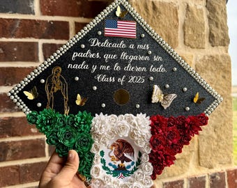 Op de afbeelding: Een afstudeerhoed versierd met de Mexicaanse vlag, bloemen en vlinders. De hoed heeft de Amerikaanse vlag en de tekst "Dedicado a mis padres, que llegaron sin nada y me lo dieron todo. Class of 2025."