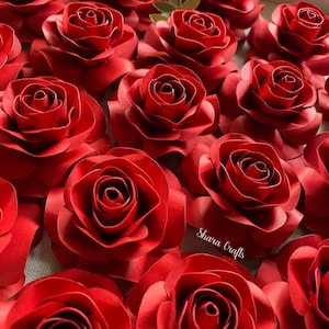 Puede incluir: Primer plano de numerosas rosas rojas de papel hechas a mano. Las rosas están hechas con pétalos detallados, mostrando un diseño realista. La imagen resalta la textura y el color vibrante de las flores. El texto "Shara Crafts" es visible.