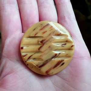 May include: A round, brown and cream-colored button with a geometric pattern. The button has a glossy finish.