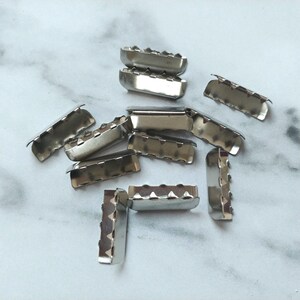 May include: A close-up of ten silver metal slider buckles. The buckles are all the same size and shape, and they have a smooth, shiny finish.