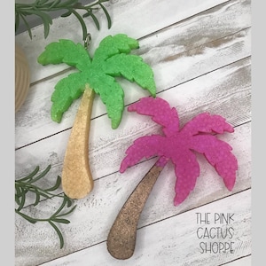 May include: Two palm tree ornaments, one with a bright green textured canopy and a tan trunk, and the other with a vibrant pink textured canopy and a brown trunk. The text THE PINK CACTUS SHOPPE is printed in black in the lower right corner.