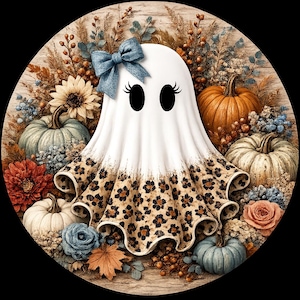 May include: A circular decorative sign featuring a white ghost with a blue bow and eyelashes, surrounded by pumpkins in shades of orange, white, and blue, along with sunflowers, roses, and dried foliage. The ghost has a leopard print pattern.