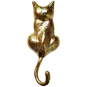 May include: A gold-colored metal cat hook with a curled tail. The cat is sitting with its back to the viewer and its tail curled into a hook shape.