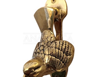 May include: A polished brass door knocker shaped like a bird with detailed wing feathers and a vertical tail. The bird is attached to a vertical mounting plate with two visible screws at the top and bottom, featuring a metallic gold finish.