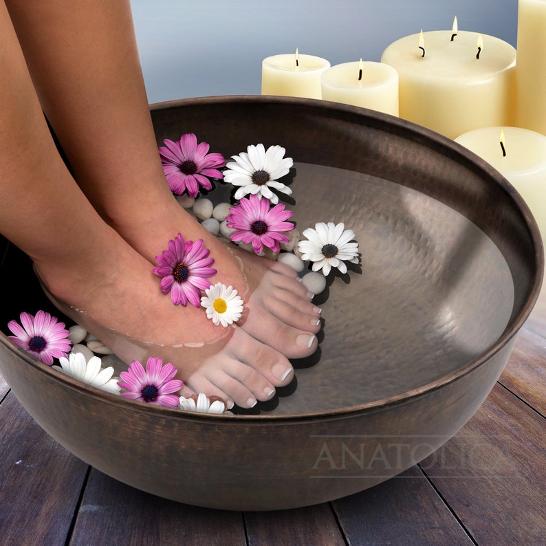 May include: A copper foot bath with water and flowers. The foot bath is on a wooden surface.