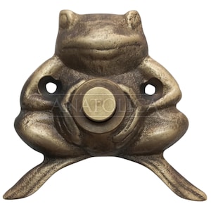 May include: A bronze-colored frog-shaped door knocker. The knocker features a detailed frog design with a circular button in the center and two eye-shaped holes. The frog's legs extend outward. The overall design is antique.