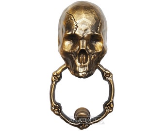 May include: A gold skull door knocker with a bone-shaped ring. The skull has a detailed design and a realistic appearance.