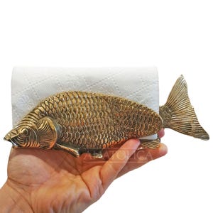 May include: A gold-coloured metal fish-shaped napkin holder. The holder is designed to hold a roll of paper towels or napkins.