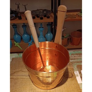 May include: A copper bucket with a hammered finish and a wooden handle. The bucket includes a matching copper ladle with a wooden handle.