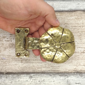 May include: A gold-toned metal door hinge with a decorative, hammered, round, flower-shaped handle.